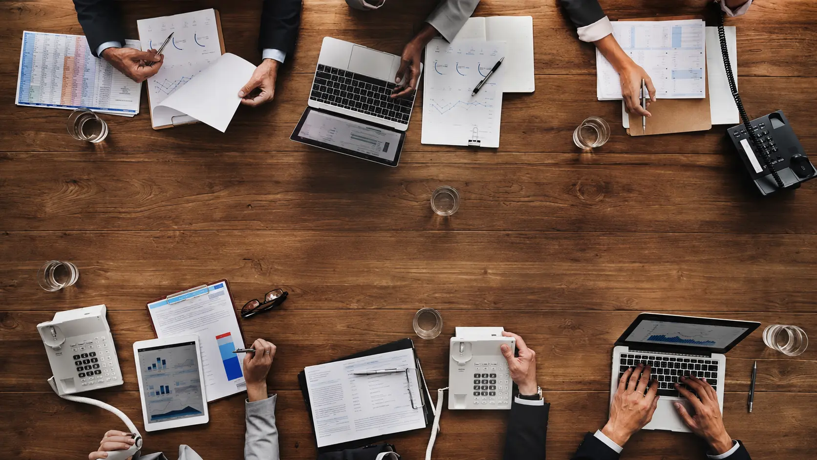 A diverse professional team collaborating around an organized table with laptops, documents, calculators, and planning materials